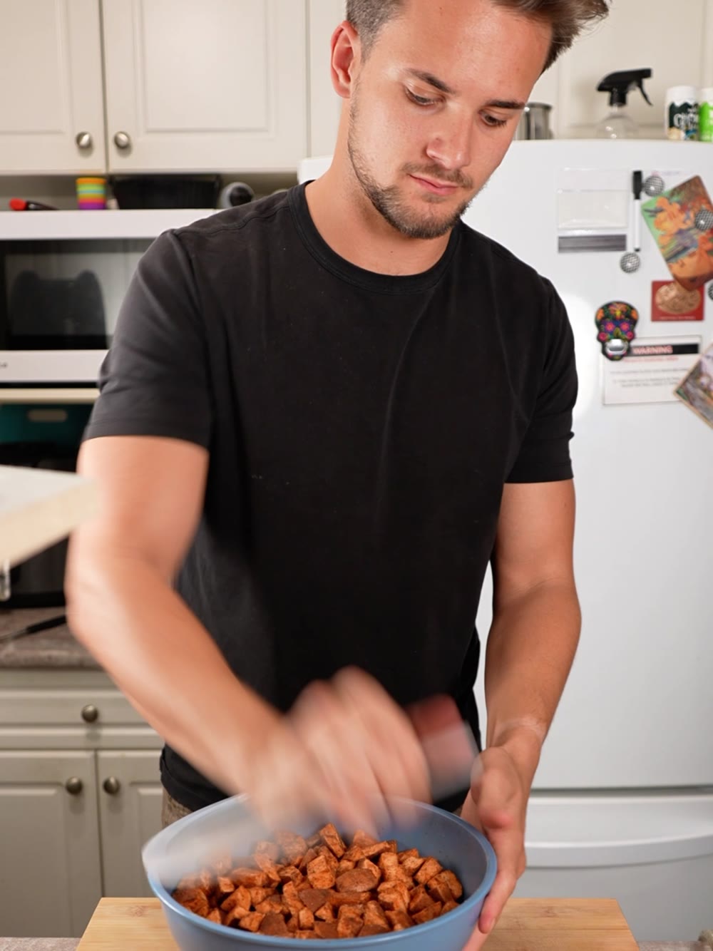 Jack tossing roasted yams in a blue bowl in his kitchen